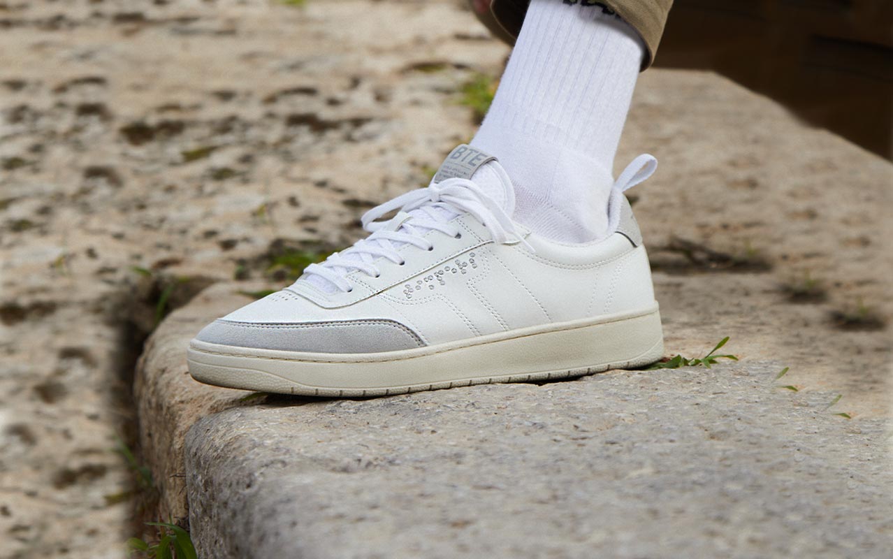 Zapatilla blanca estilo años 80 con detalles en gris. Aparece Braille en el lateral.