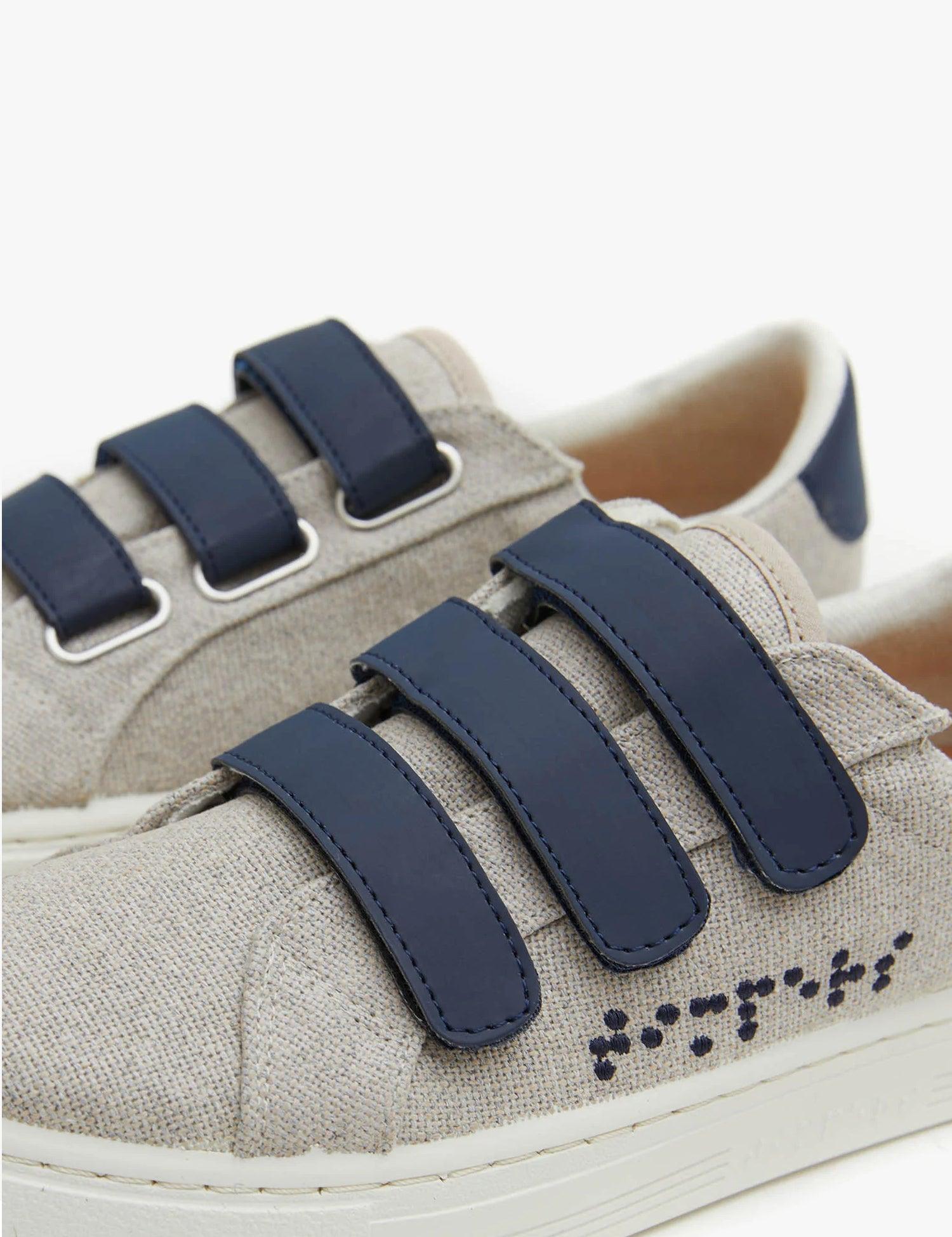 Velcro Crude de color gris, con suela blanca y 3 tiras de velcro en color azul marino. 
